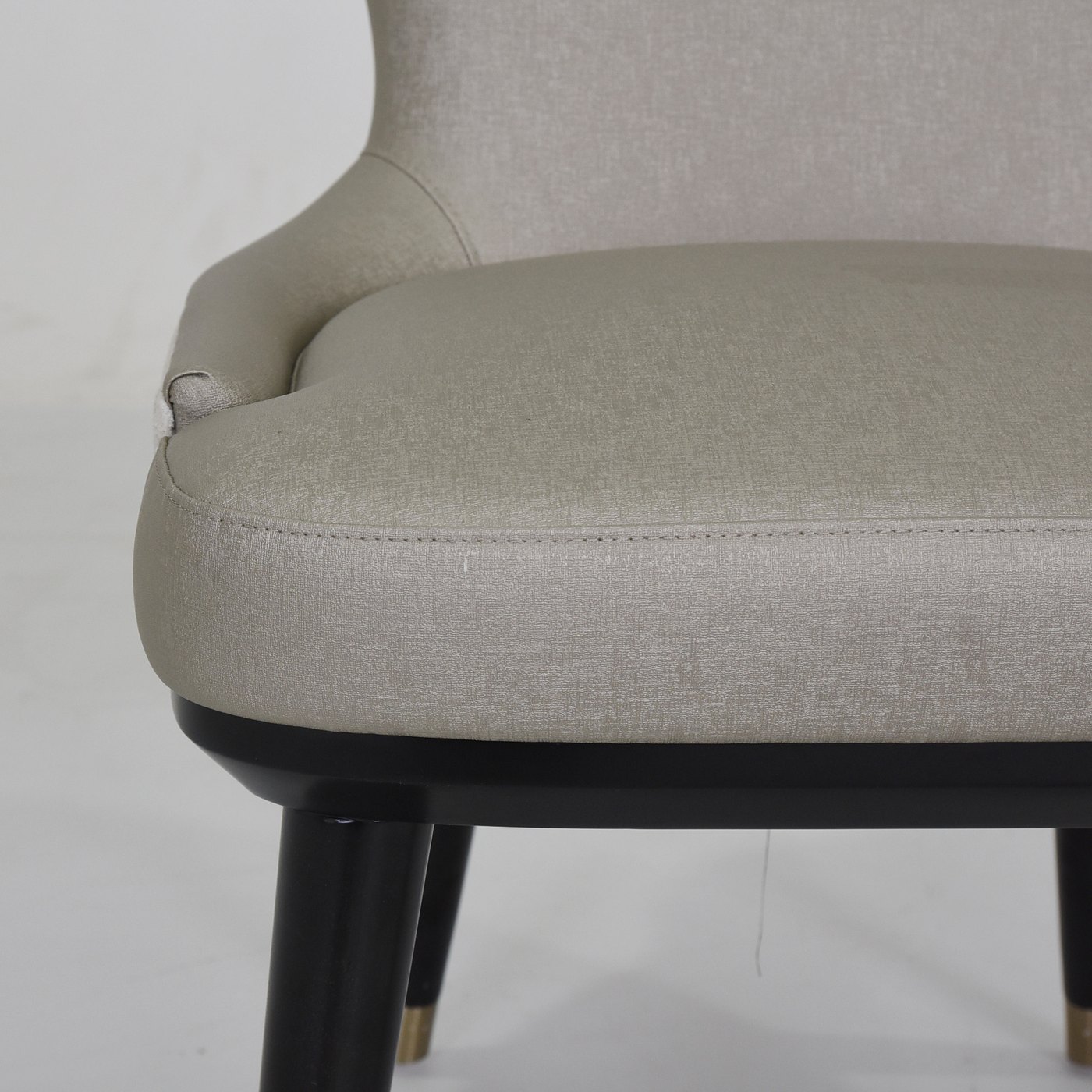 Close view of an upholstered chair seat edge, piping, seam and dark leg