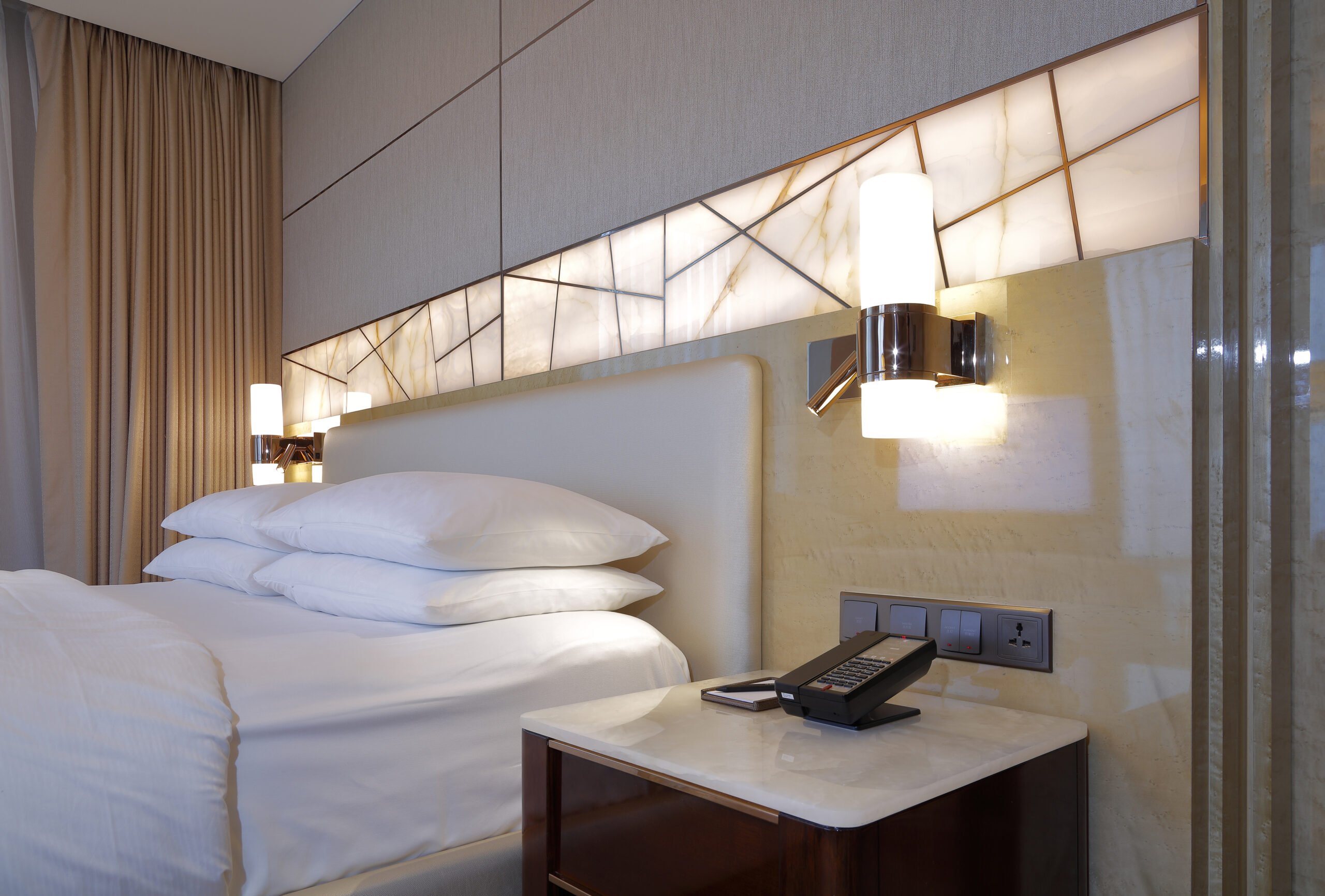 Hotel bedside area with headboard, bedside table, lighting and power interfaces
