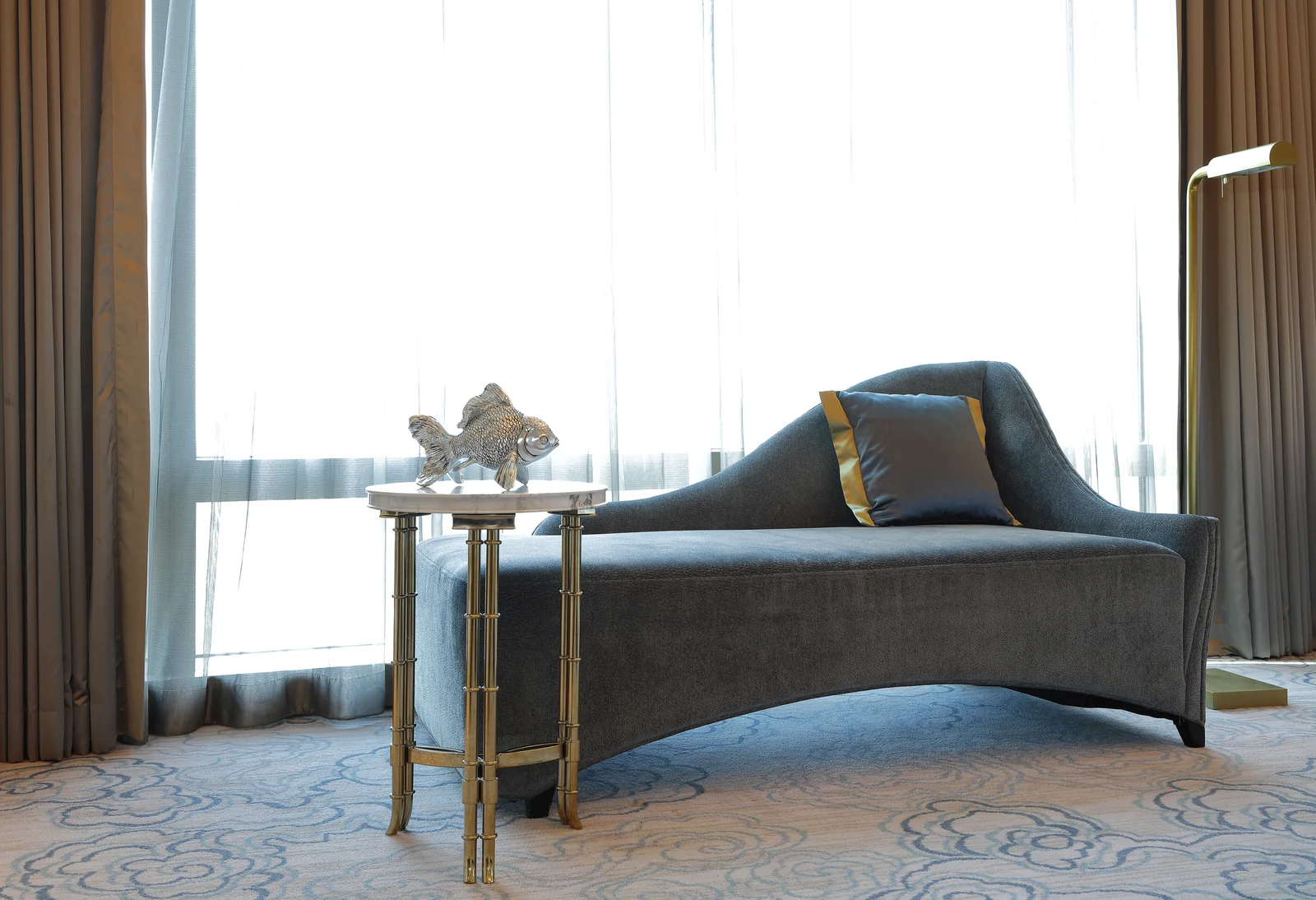 Blue upholstered hotel chaise with cushions and a side table