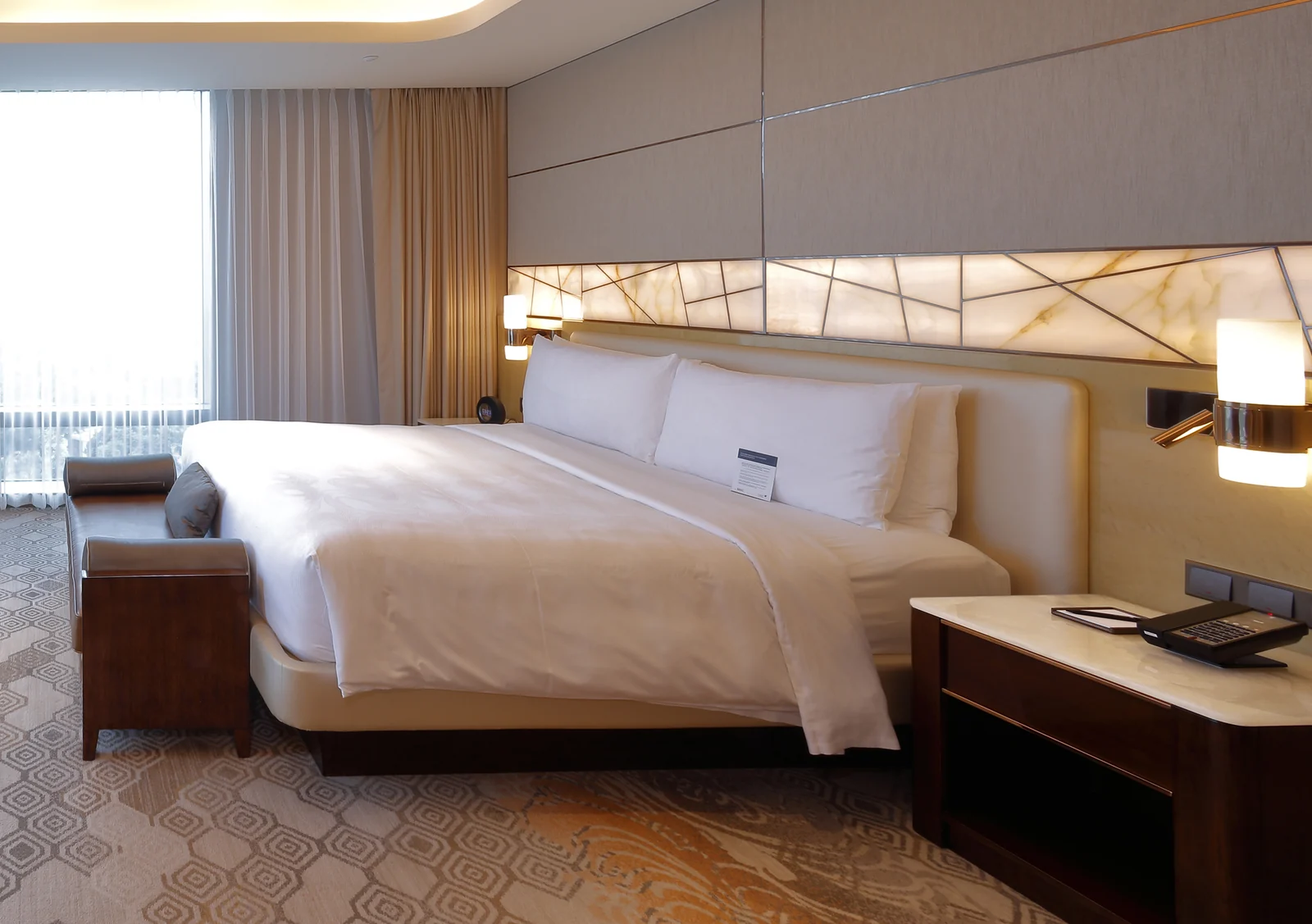 Hotel guestroom with bed, upholstered bench, bedside furniture and wall panels