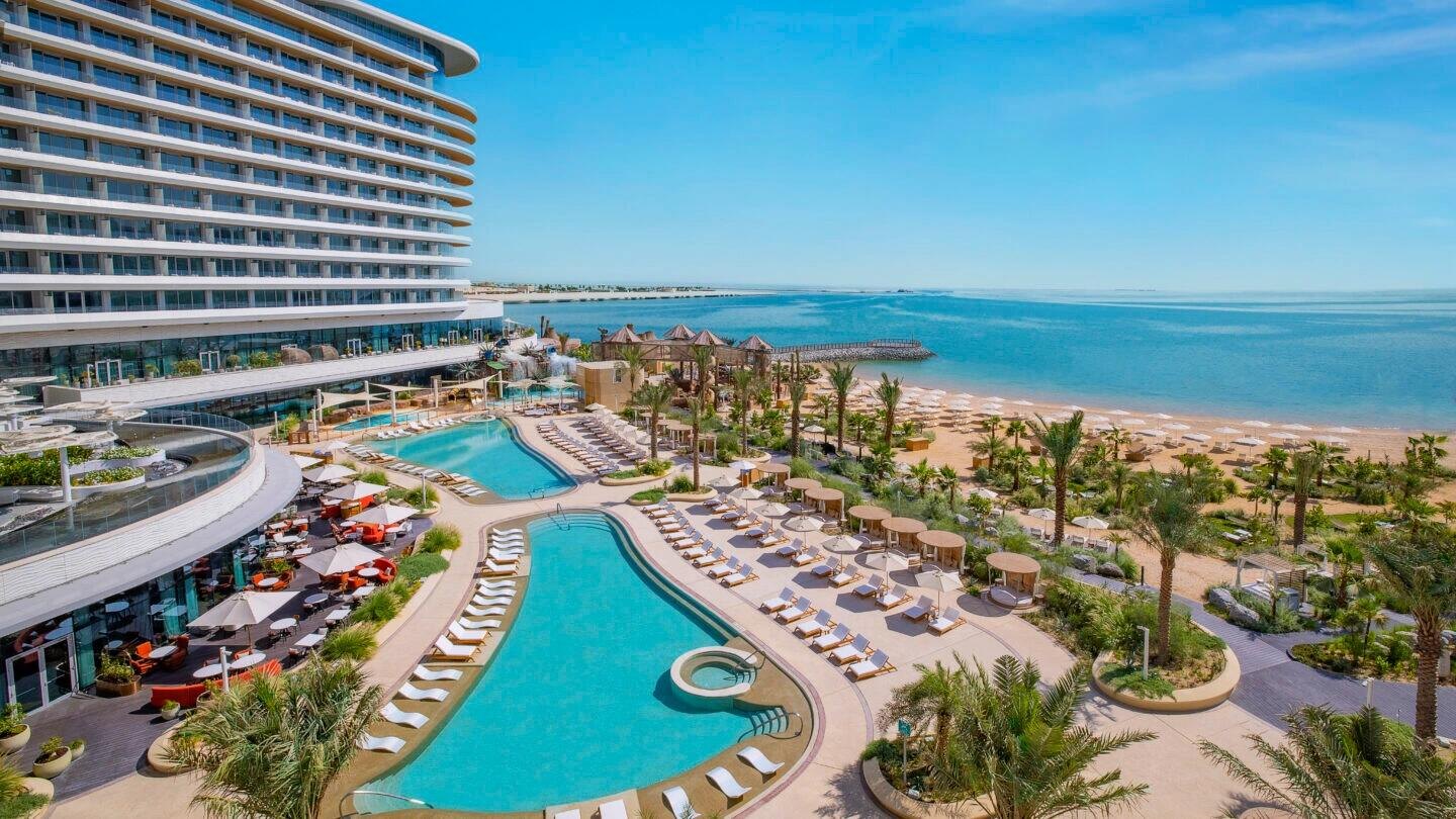 Wide coastal hospitality site with beach, pools, loungers, cabanas and dining terraces