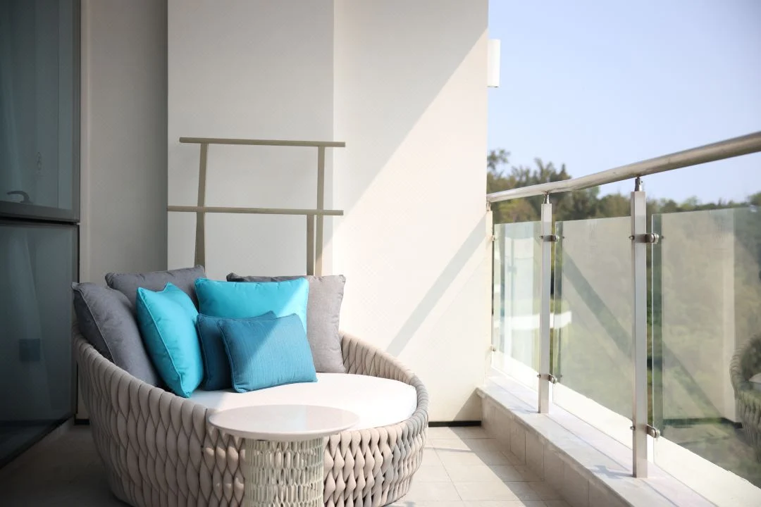 Sheltered hotel balcony with a woven daybed, small table and loose cushions