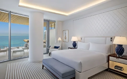 Hotel guestroom opening to a balcony with outdoor chairs beside the waterfront