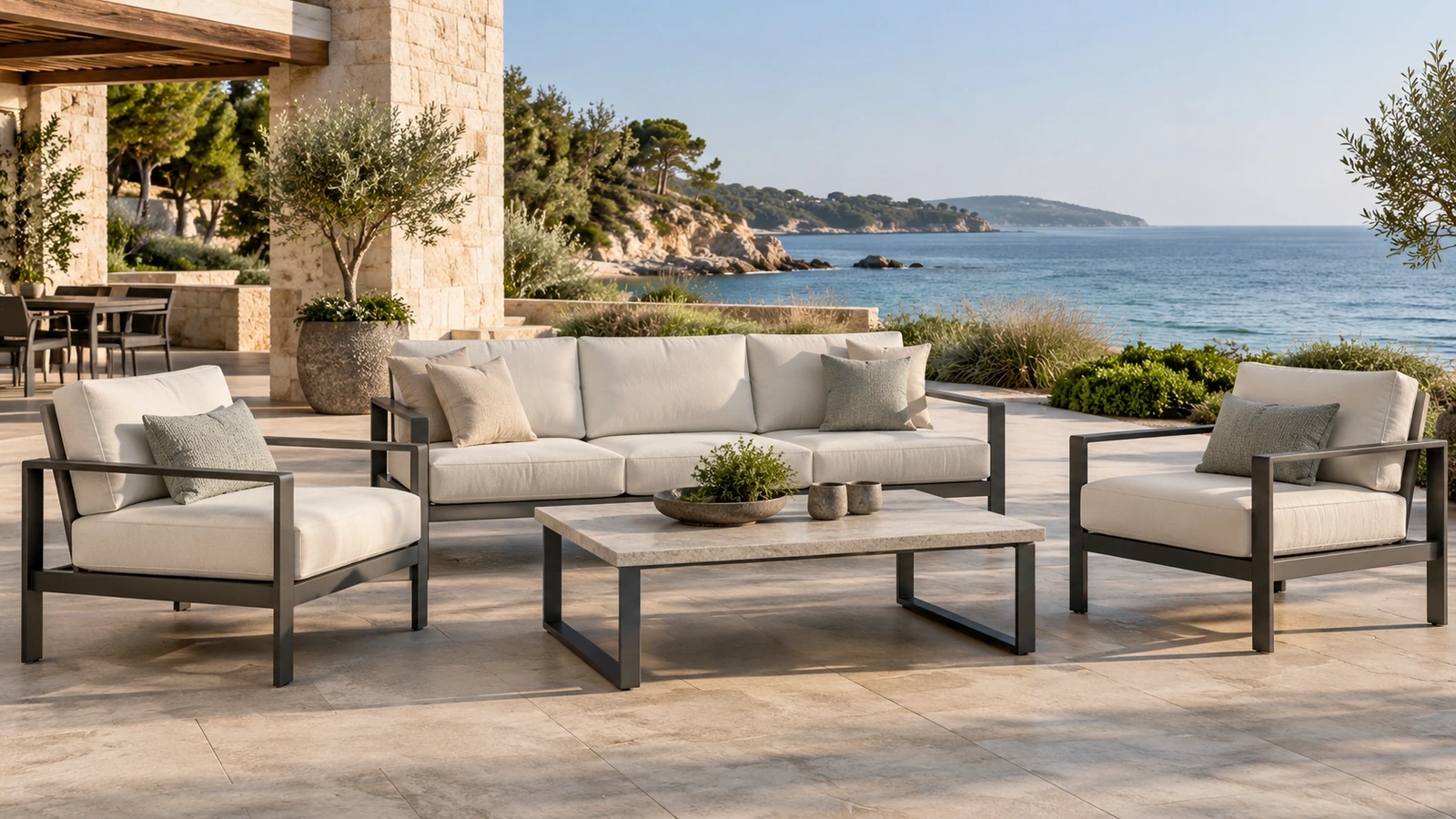 Outdoor lounge chairs and a sofa on a coastal hotel terrace overlooking the sea.