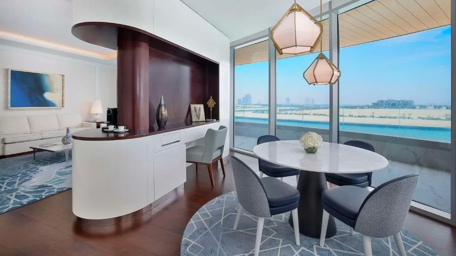 Round dining table with a central pedestal surrounded by four chairs in a hotel suite.