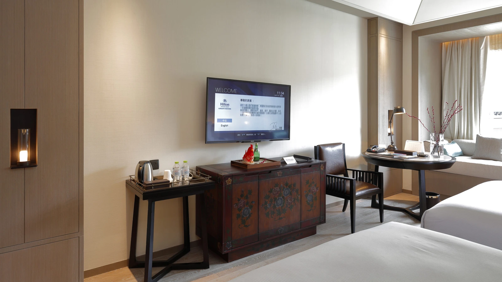 Hotel guestroom storage cabinet beside a work table and seating